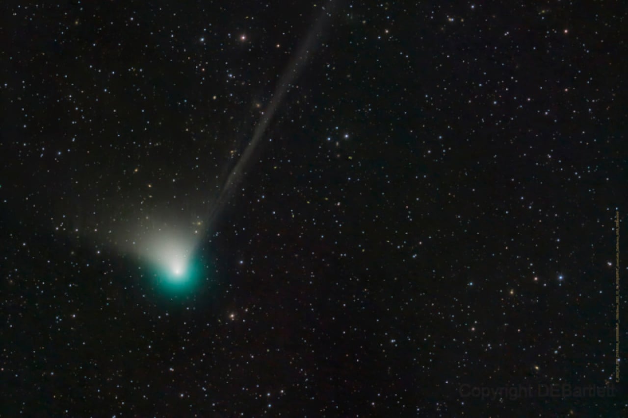 A green comet with a fuzzy table is visible against a background of stars A green comet with a fuzzy table is visible against a background of stars